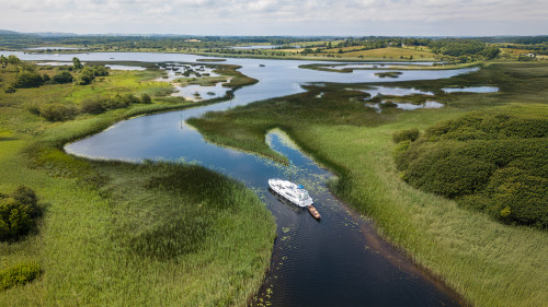 Aerial view of a white cruiser boat sailing through winding marshes on the River Shannon.