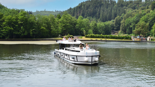 Horizon boat gliding across a calm lake surrounded by lush forest and distant hills in Alsace.