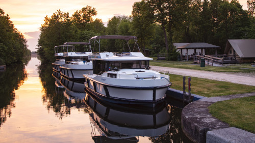Several Horizon boats are moored along the Rideau Canal beside a small campground under a pink sunset sky.