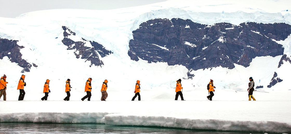 Guests in yellow parkas walk in a single file during a sea ice landing