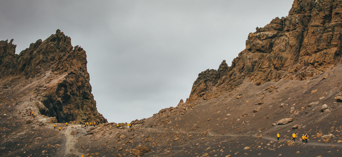 Guests in yellow parkas follow other guests up a hill at Deception Island, Antarctica.