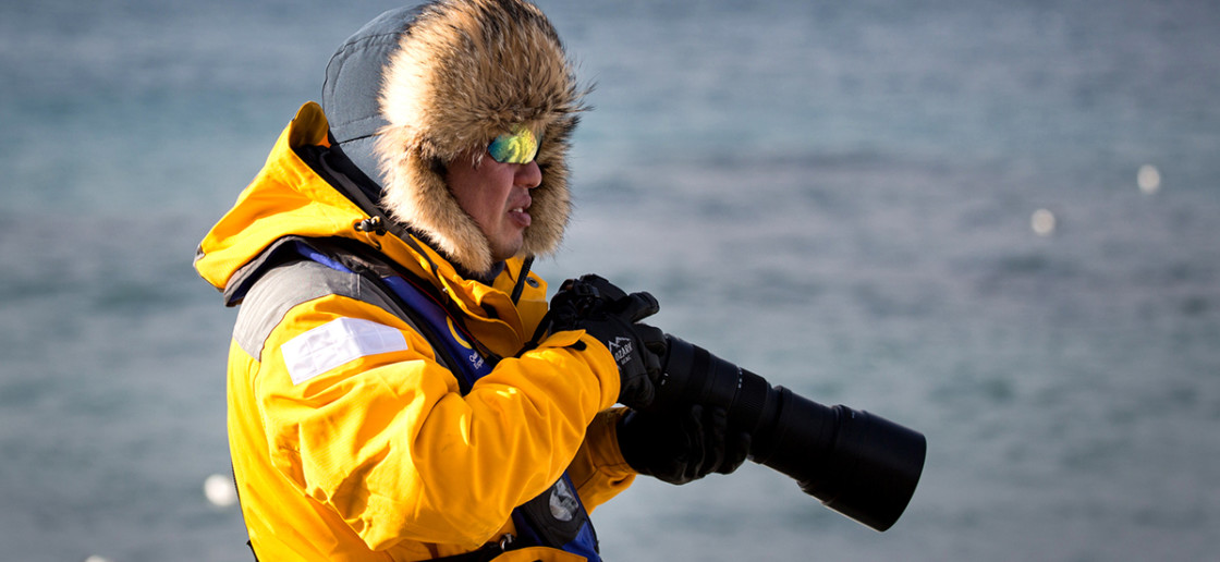 A guest in a yellow parka uses their telephoto lens during a landing in the Antarctic Peninsula.