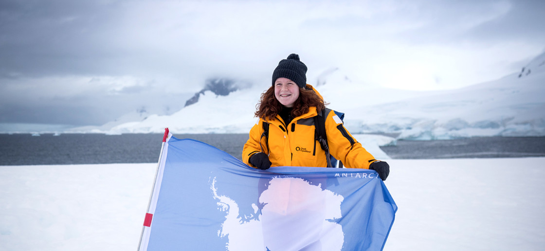 A guest poses with our Antarctic flag with the snowy peaks in the background