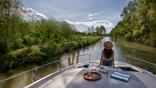 Tranquil view from the boat as a woman lounges under blue skies on a scenic river cruise.