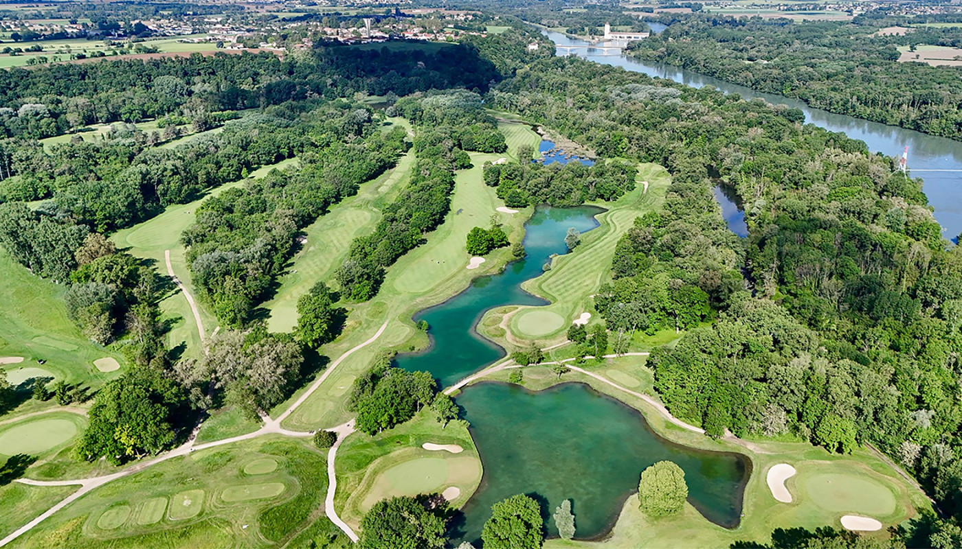 An aerial view of fairways and bunkers running between tree lines around a lake at Golf Club de Lyon in Lyon, France.