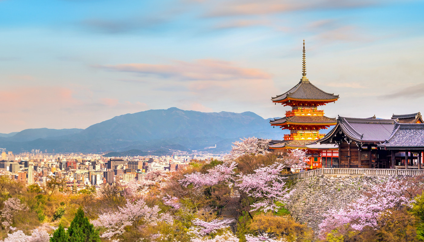 The Kiyomizu-dera Temple overlooks the city skyline of Kyoto, Japan with mountains in the distance.