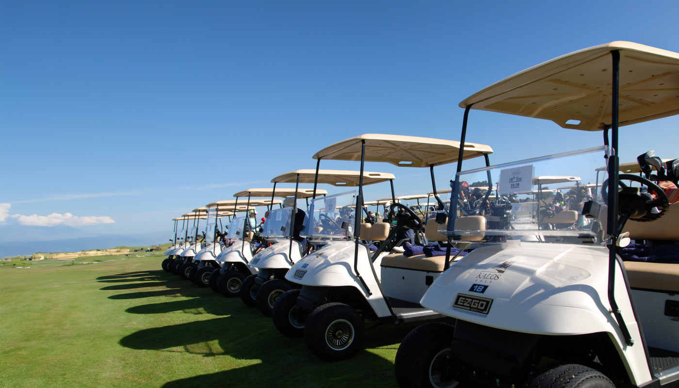 A line of golf carts prepared for Kalos golfers at a golf course under clear blue sky.