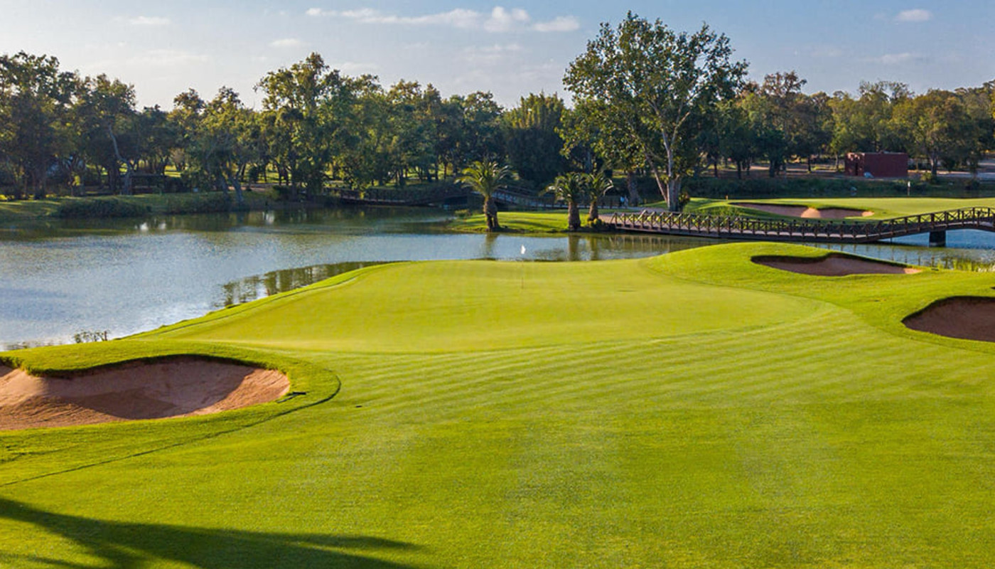 A green sits at the edge of a large lake, surrounded by trees, with a bridge in the distance at Royal Golf Dar Es Salam in Rabat, Morocco.