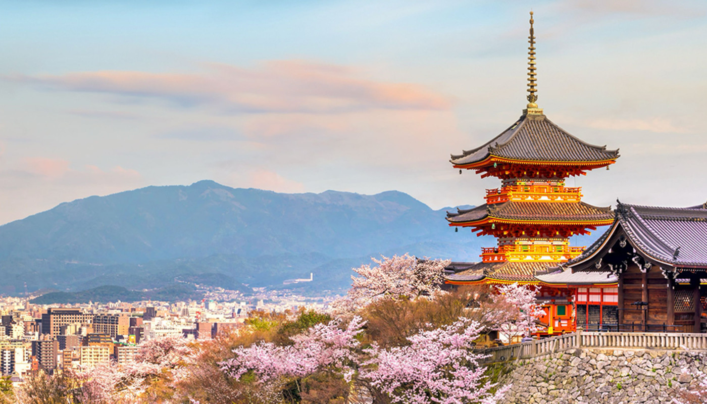 The Kiyomizu-dera Temple overlooks the city skyline of Kyoto, Japan with mountains in the distance.