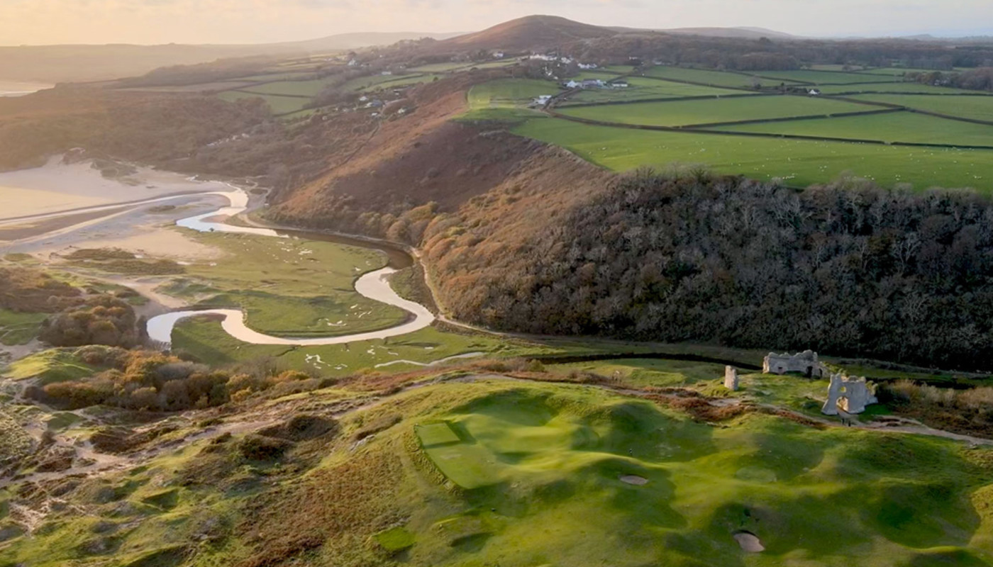 An aerial view of Royal Porthcawl Golf Club winding along the hilly coast of Wales under soft evening sunlight.