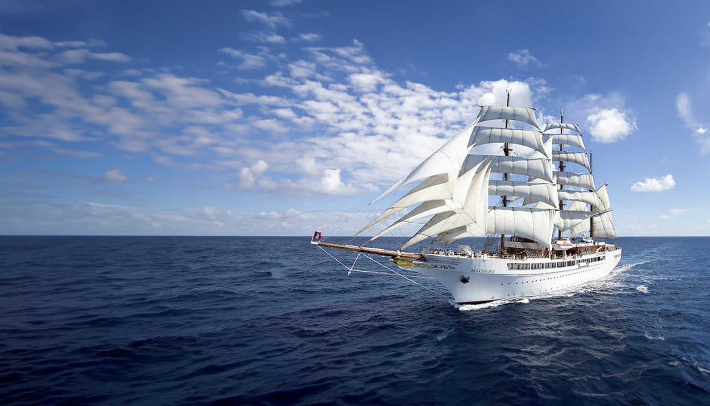 Sea Cloud II sailing on calm blue water under a cloud-streaked sky.