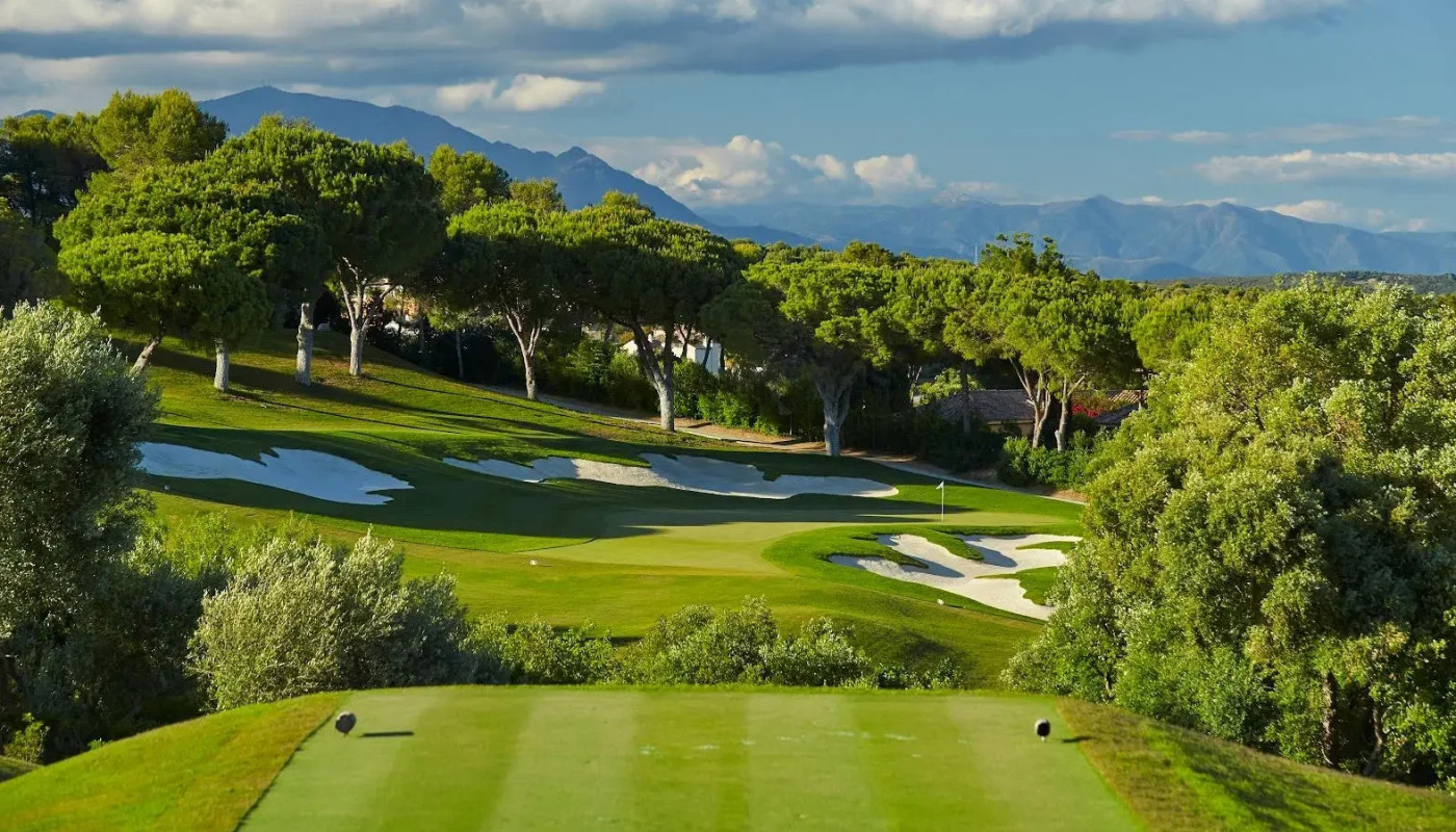 A tee box view of the 15th hole green at Real Club Valderrama framed by mountains in the distance in Sotogrande, Spain.