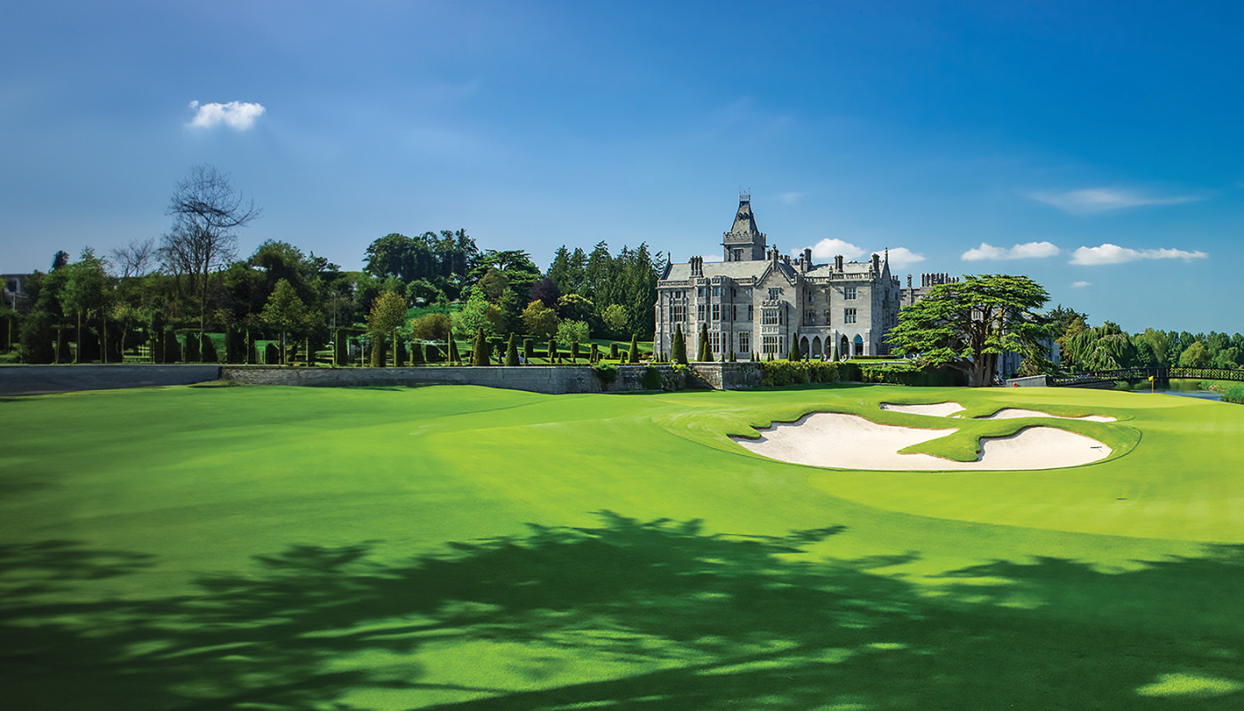 A view of the 18th hole green, manor house, and gardens surrounded by trees at Adare Manor in Limerick, Ireland.