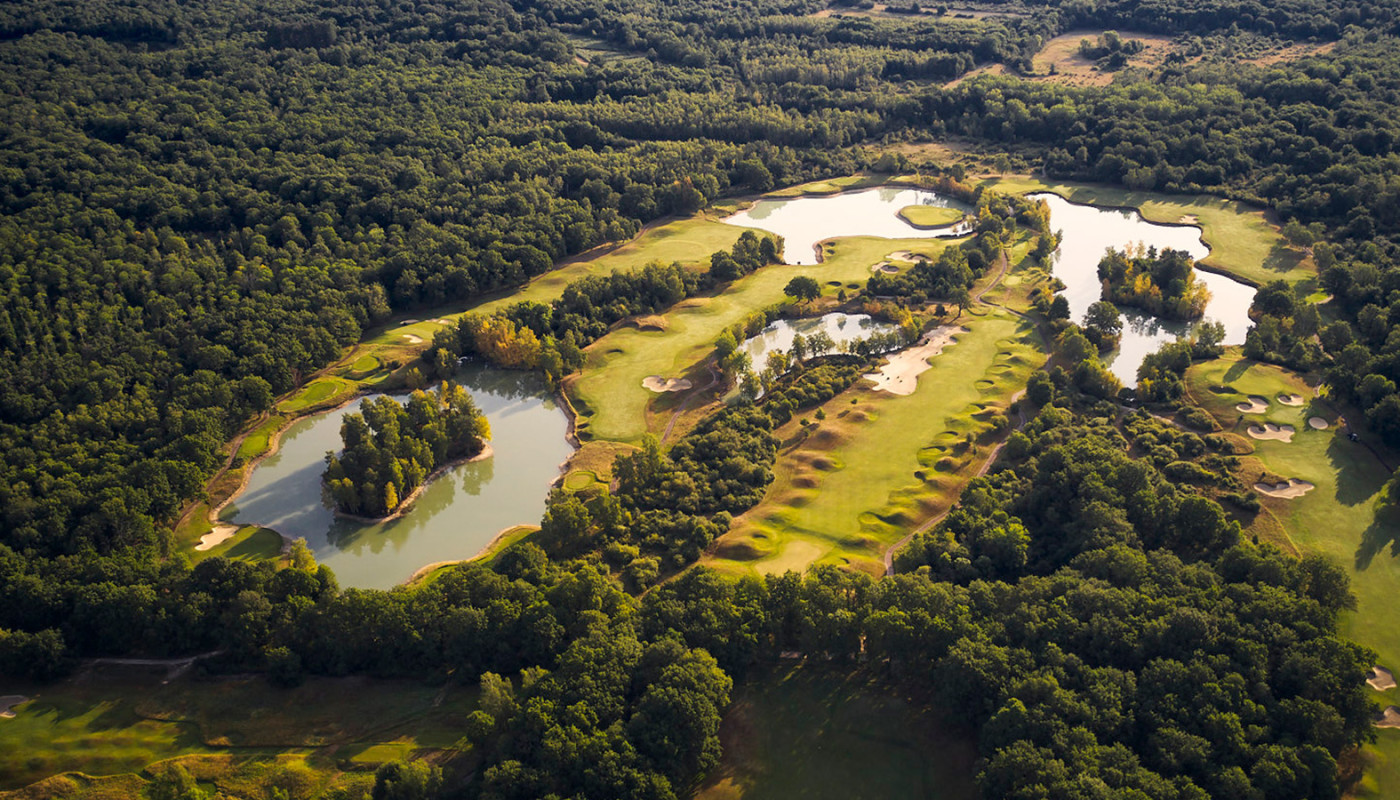 An overhead view of winding fairways cutting through trees and small lakes at Les Bordes Golf Club in France.