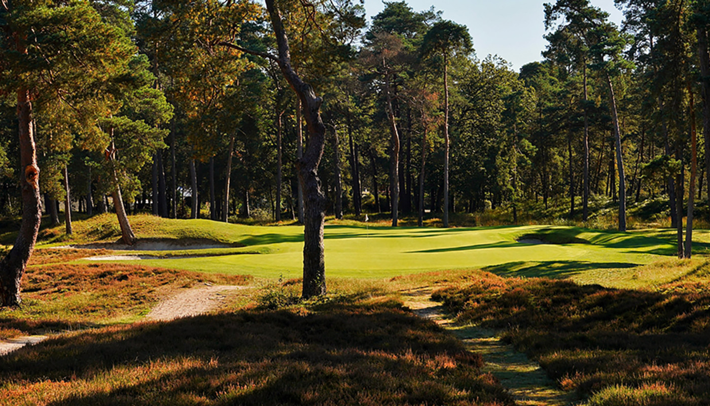 The fairway and green of a hole at Morfontaine Golf Club surrounded by fall-colored dense forest in Morfontaine, France.