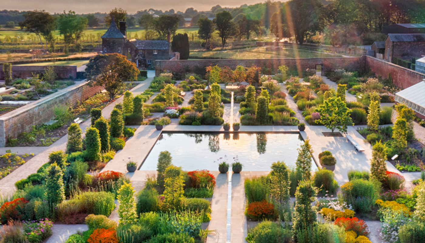 Sunrays shine reflect off a pond surrounded by pristine flowers and hedges at RHS Garden Bridgewater in Manchester, England.