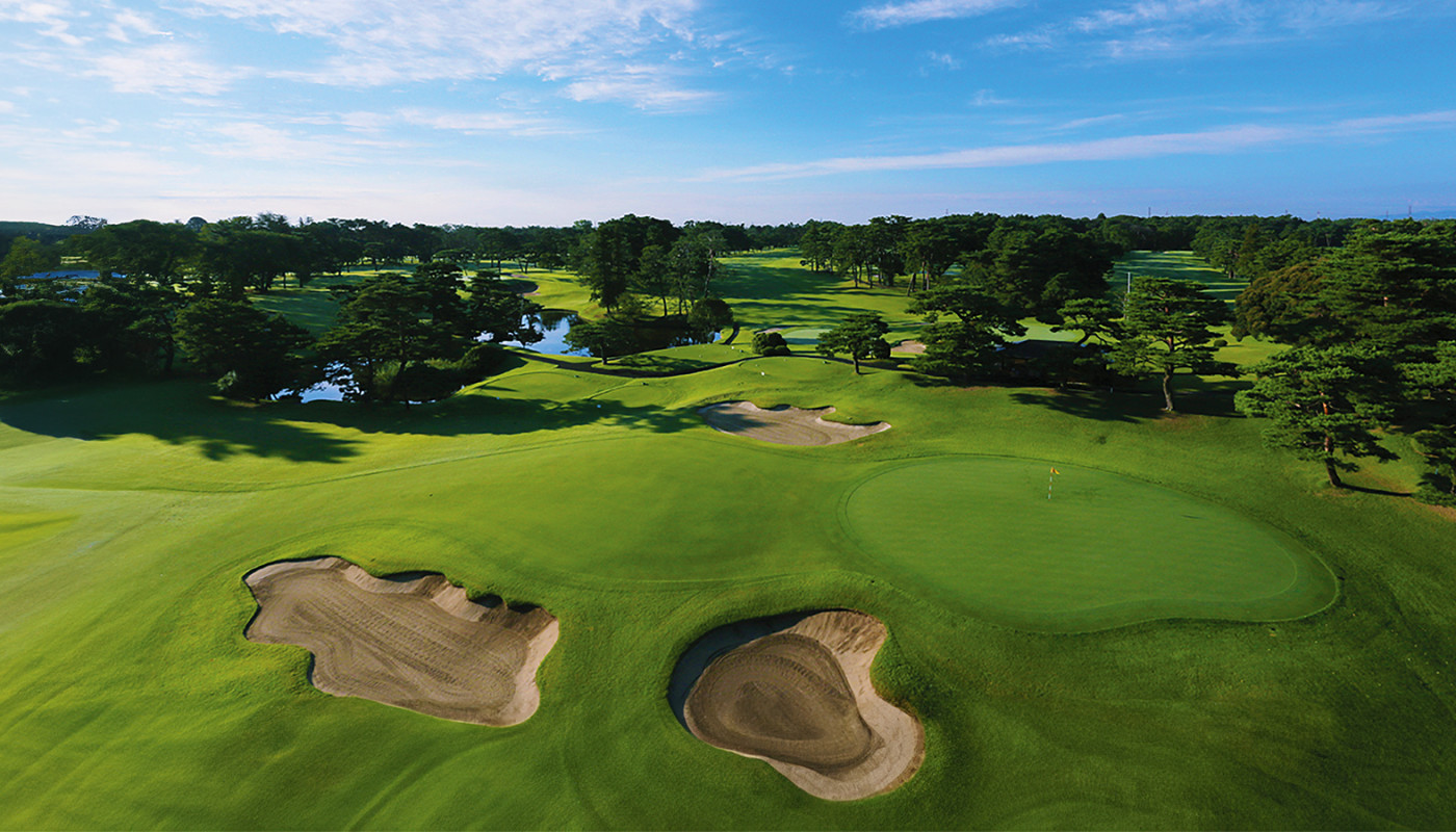 An overhead view of a green surrounded by bunkers under a clear blue sky at Kasumigaseki Country Club in Tokyo, Japan.