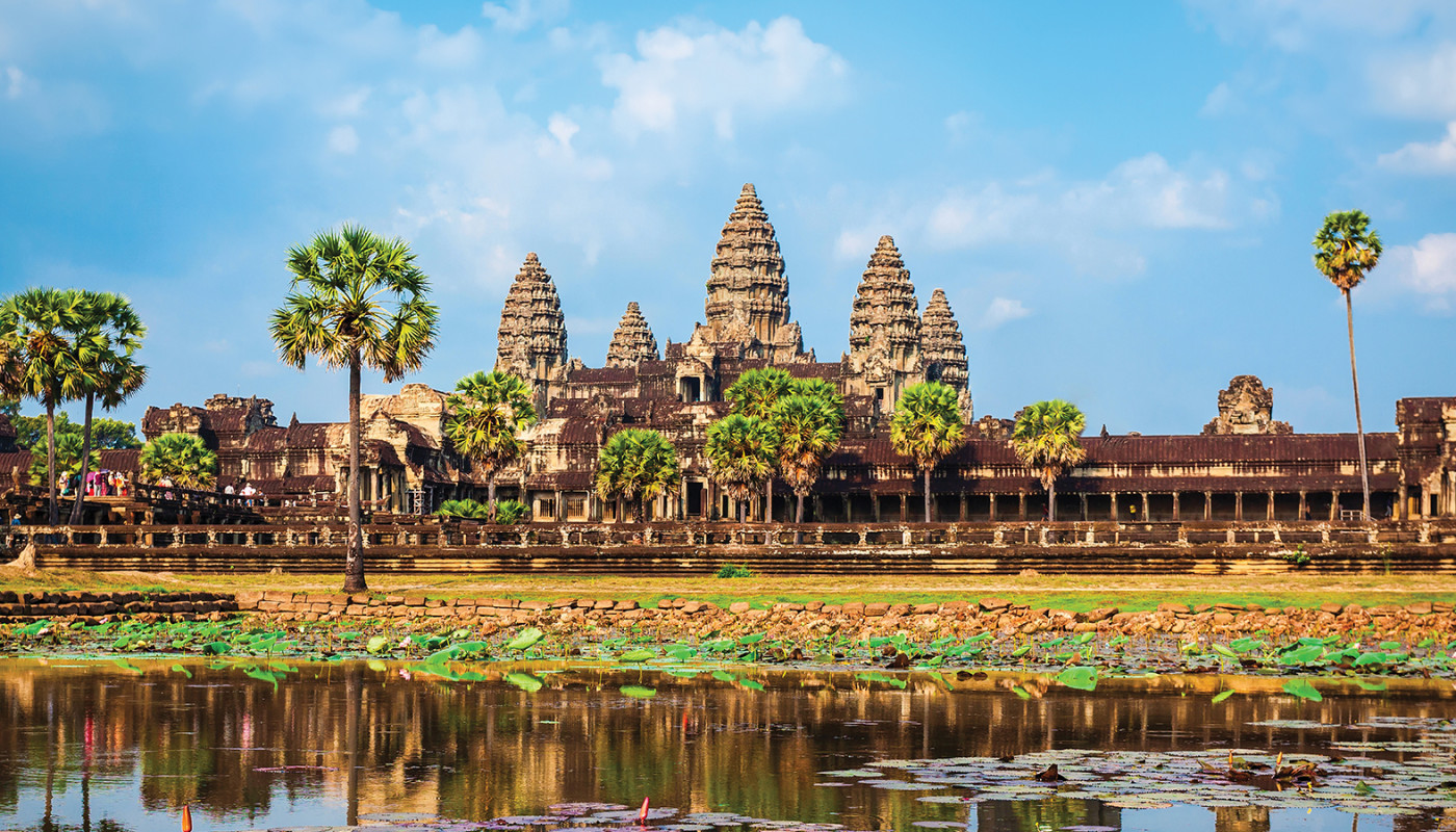 A view of Angkor Wat temple surrounded by palm trees reflecting off a lake in Siem Reap, Cambodia.