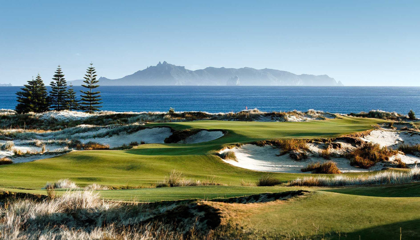 A tee box view of a green, surrounded by bunkers, along the coast of the Pacific Ocean at Te Arai Links in Tomarata, New Zealand.