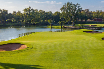 A green sits at the edge of a large lake, surrounded by trees, with a bridge in the distance at Royal Golf Dar Es Salam in Rabat, Morocco.