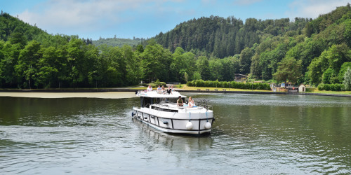 Horizon‑Boot gleitet über einen ruhigen See, umgeben von üppigem Wald und fernen Hügeln im Elsass.