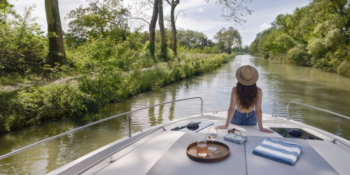 Une femme tranquillement assise à l'avant du bateau, qui regarde la rivière avec des arbres.