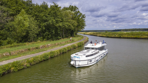 Horizon boot vaart een rustige bocht, omgeven door bos en met gras begroeide paden onder een deels bewolkte lucht in de Elzas.