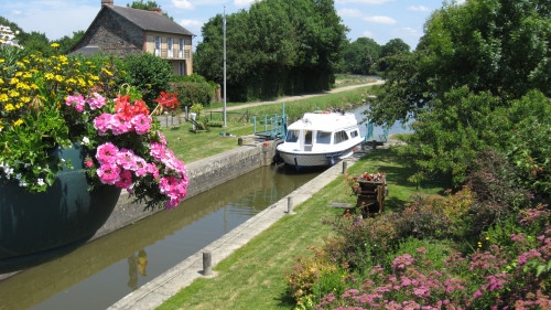 Sfeervolle sluis met kleurrijke bloemen op de voorgrond en een groen landschap daarachter.