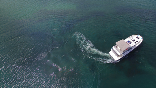 Aerial view of a motorboat cruising across open water, leaving a curved wake behind