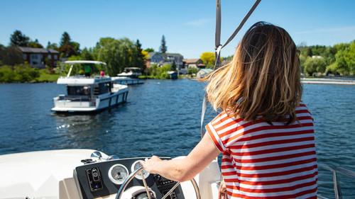 Jonge vrouw aan het roer van een Horizon-boot van Le Boat tijdens de nadering van de jachthaven van Westport op Big Rideau Lake, Westport, Ontario, Canada.