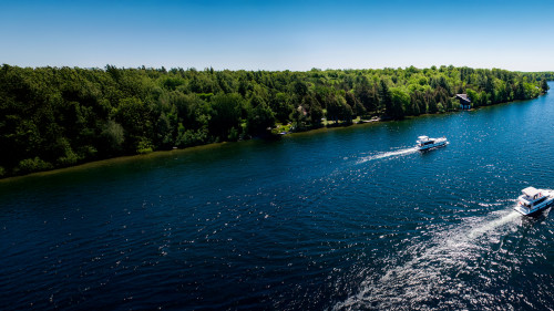 Two Horizon boats cruising side by side along a green shoreline on the Rideau Canal in Ontario under a clear sky