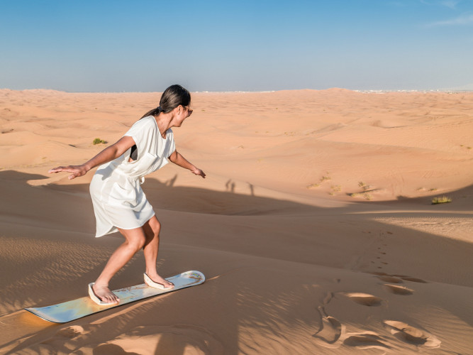 Frau auf einem Sandboard in einer Dünenlandschaft