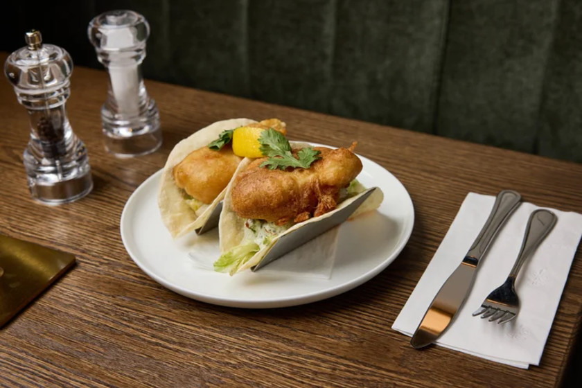 Tacos de poisson servis sur une table dans un restaurant, accompagnés de garnitures fraîches et présentés dans une ambiance conviviale