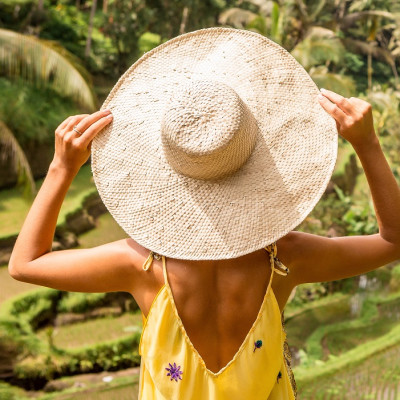 Is Indonesia safe? Beautiful young lady in shine through dress touch straw hat. Girl walk at typical Asian hillside with rice farming, mountain shape green cascade rice field terraces paddies. Ubud, Bali, Indonesia