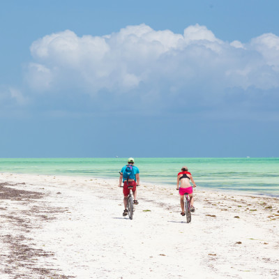 Tourist couple cycling down picture perfect white sand tropical beach of Paje village, Zanzibar, Tanzania, Africa