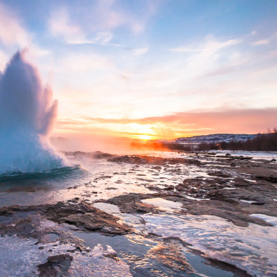 Eruption of Strokkur geyser in Iceland. Winter cold colors, sun lighting through the steam