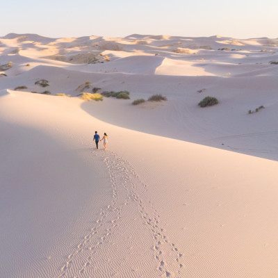 Romantic latin couple walking in the white dunes desert leaving footprints behind them. Samalayuca, Chihuahua, Mexico. Aerial shot