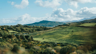 Panoramic view of lush green hills and distant peaks under a bright Irish sky.