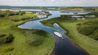 Aerial view of a white cruiser boat sailing through winding marshes on the River Shannon.