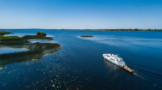 White cruiser boat towing a wooden canoe on Lough Key under clear blue skies.