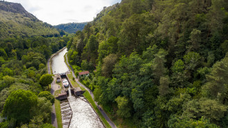 Bateau entrant dans une écluse nichée dans une vallée forestière luxuriante au pied des Vosges.