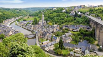 Stone heritage bridge crossing the river in Dinan, surrounded by historic riverside houses and lush hills.