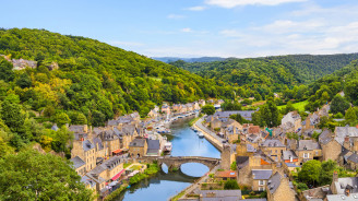 Historic town of Dinan nestled along the river, with stone buildings, surrounding hills, and natural greenery.