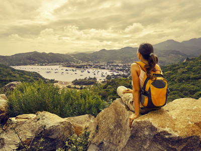 Woman traveler looks at the edge of the cliff on the sea bay of mountains in the background