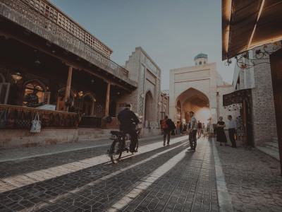 Belebte Altstadtgasse in Usbekistan mit historischen Backsteingebäuden, einem Torbogen und Passanten bei warmem Abendlicht.