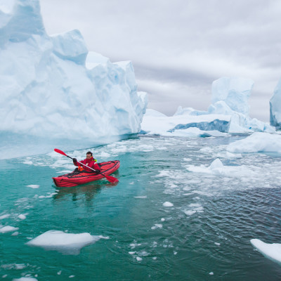 Man paddling on kayak between ice in Antractica, near Pleneau Island