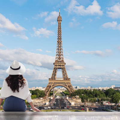 Young traveler woman in white hat looking at Eiffel tower, famous landmark and travel destination in Paris, France in summer