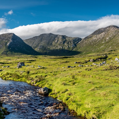 Connemara landscape in Ireland - a river flows amid the meadows in front of the majestic Twelve Bens mountains