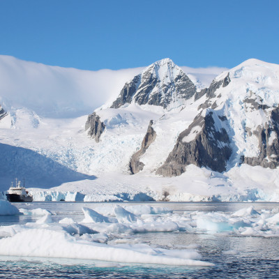 A small passenger vessel stands between icebergs with a spectacular view of the mountains of Antarctica