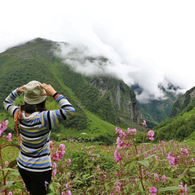 Young female climber walking down grassy rocky hill in green beautiful mountains in india